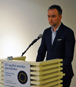 En mann (Jurist Eirik Holmøyvik) snakker ved en talerstol med teksten "EU og det norske paradoks".