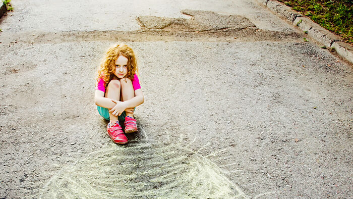 A little girl sitting on the ground with her knees to her chest.