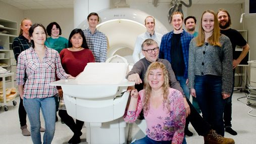 A group of people posing in front of a magnetic resonance imaging scanner. 