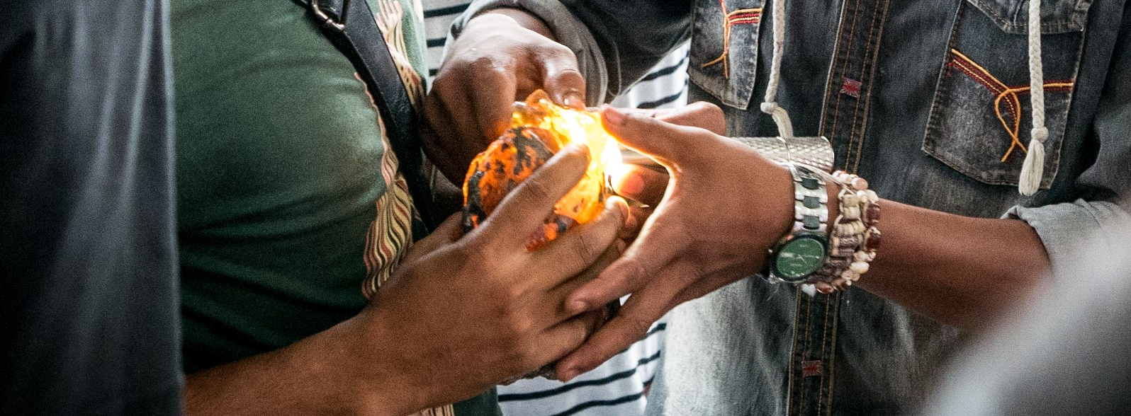 Two people holding a lump of amber between them in their hands, one of them is shining light into the amber with a flashlight causing it to glow