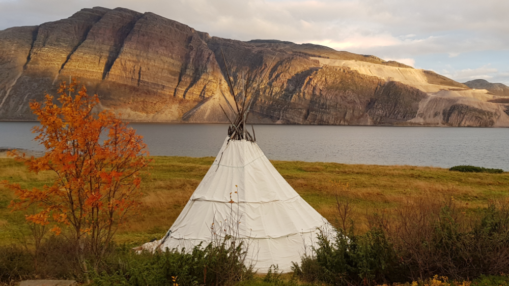 Tent by a lake, where there is an extractive site behind the mountain in the distance