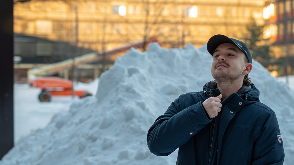 Martin Aktmyr i ferd med å dra glidelåsen opp på jakka foran stor snøhaug